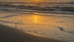 A beach with waves, a sunset, and a clear sky.