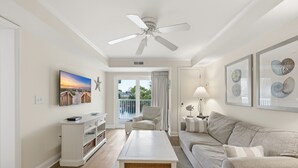 A living room with a ceiling fan, a sofa, a coffee table, a TV, and framed artwork.