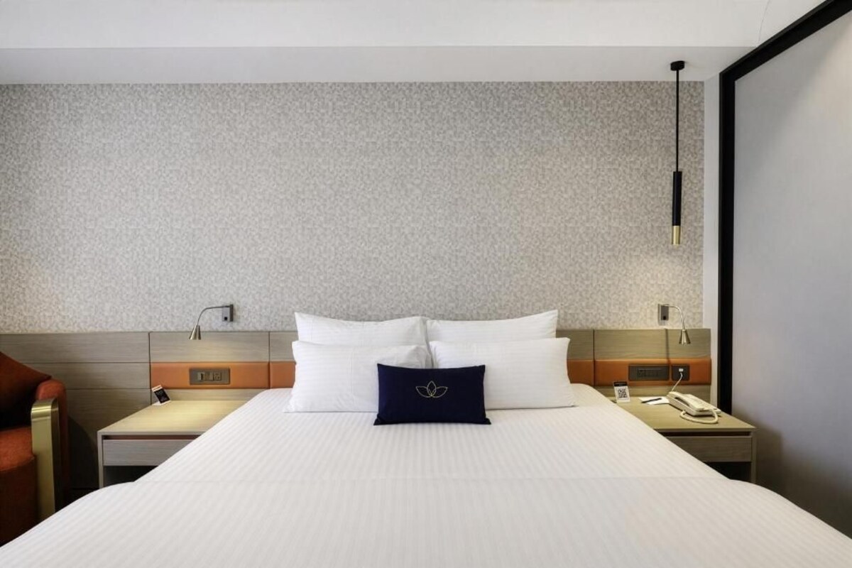 A hotel room with a bed, two bedside tables, a nightstand, a lamp, and a chair.