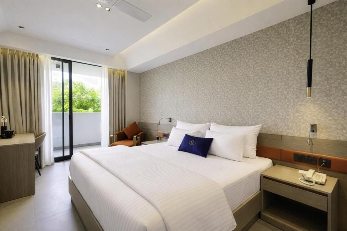 Une chambre d’hôtel avec un grand lit, un bureau, une chaise, une table de chevet avec un téléphone et une vue sur l’extérieur, accessible par une porte coulissante.