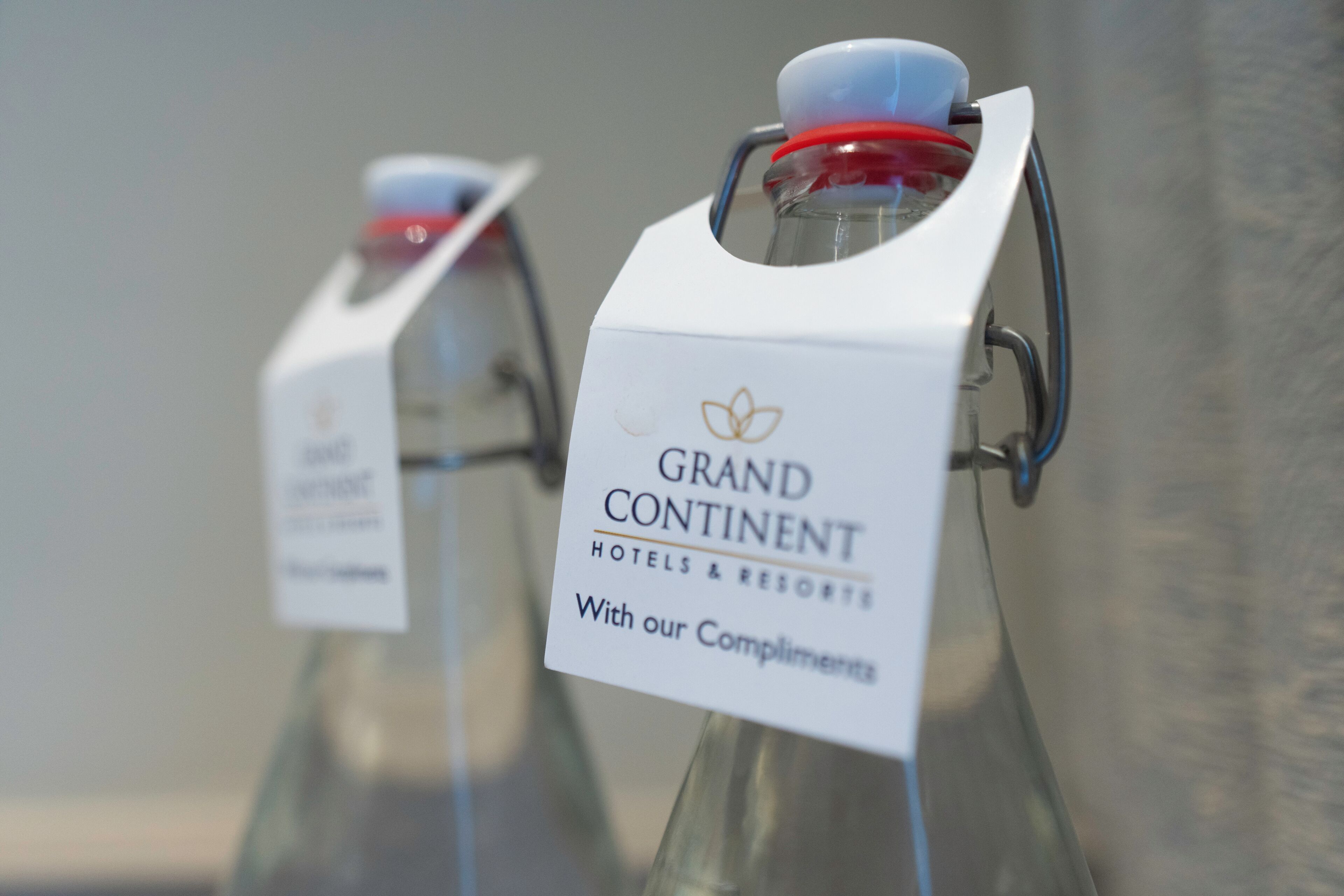 Two glass bottles with white labels, one reading 'GRAND CONTINENT HOTELS & RESORTS' and the other 'With our Compliments.'