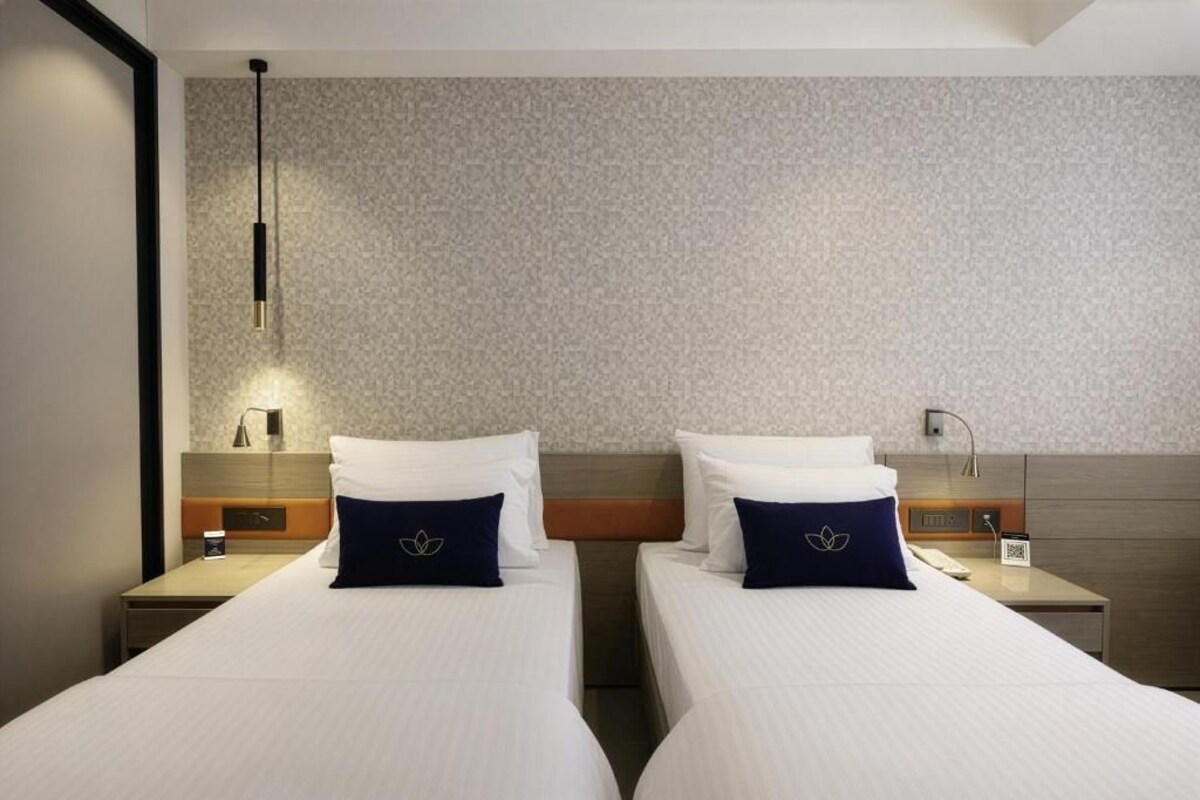 A hotel room with two beds, a nightstand with a lamp, and a wall-mounted light fixture.