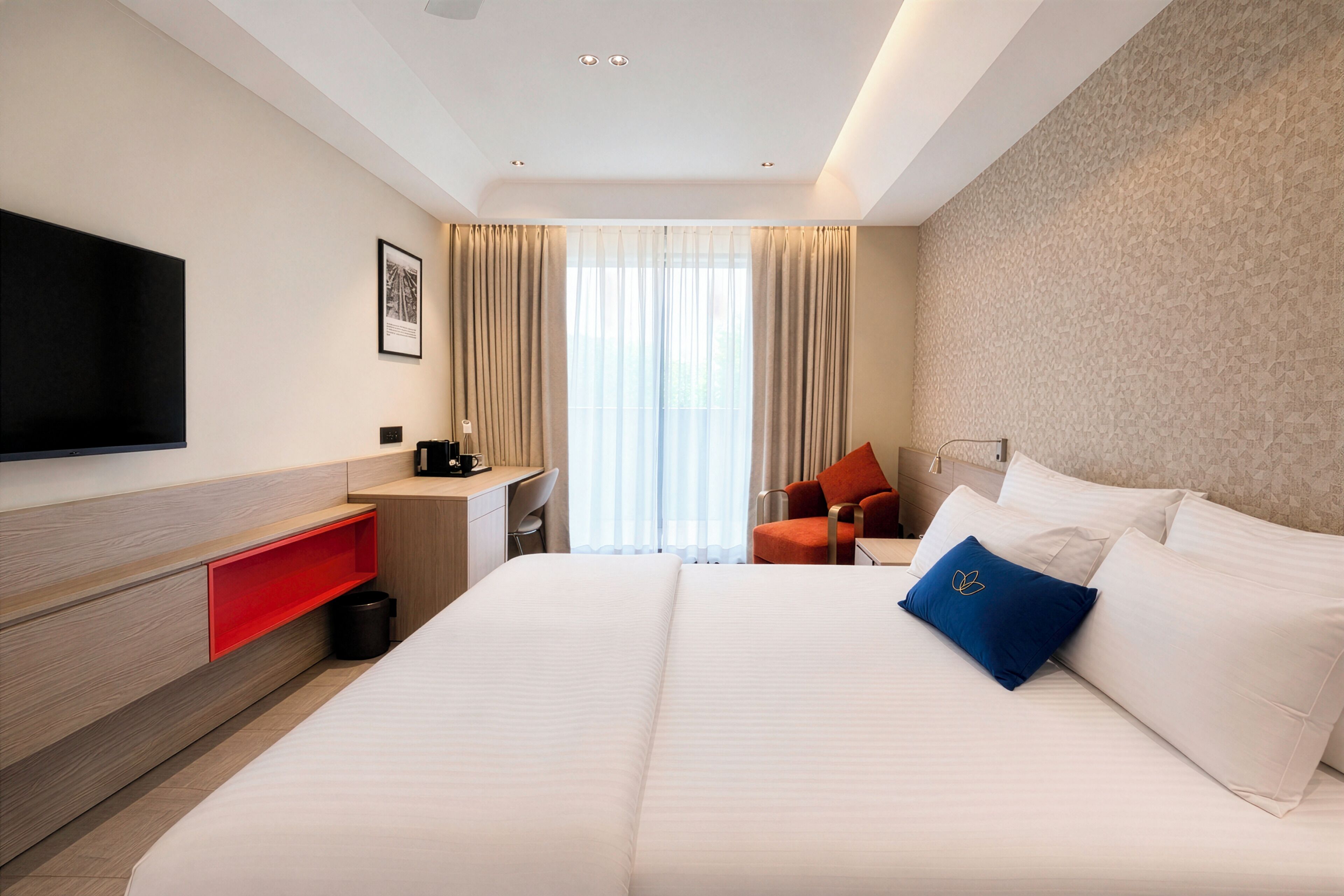 Quarto de hotel com cama, escrivaninha, cadeira, televisão e janela com cortinas.