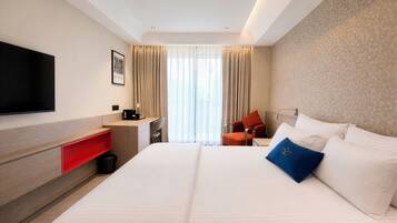 A hotel room with a bed, a desk, a chair, a TV, and a window with curtains.