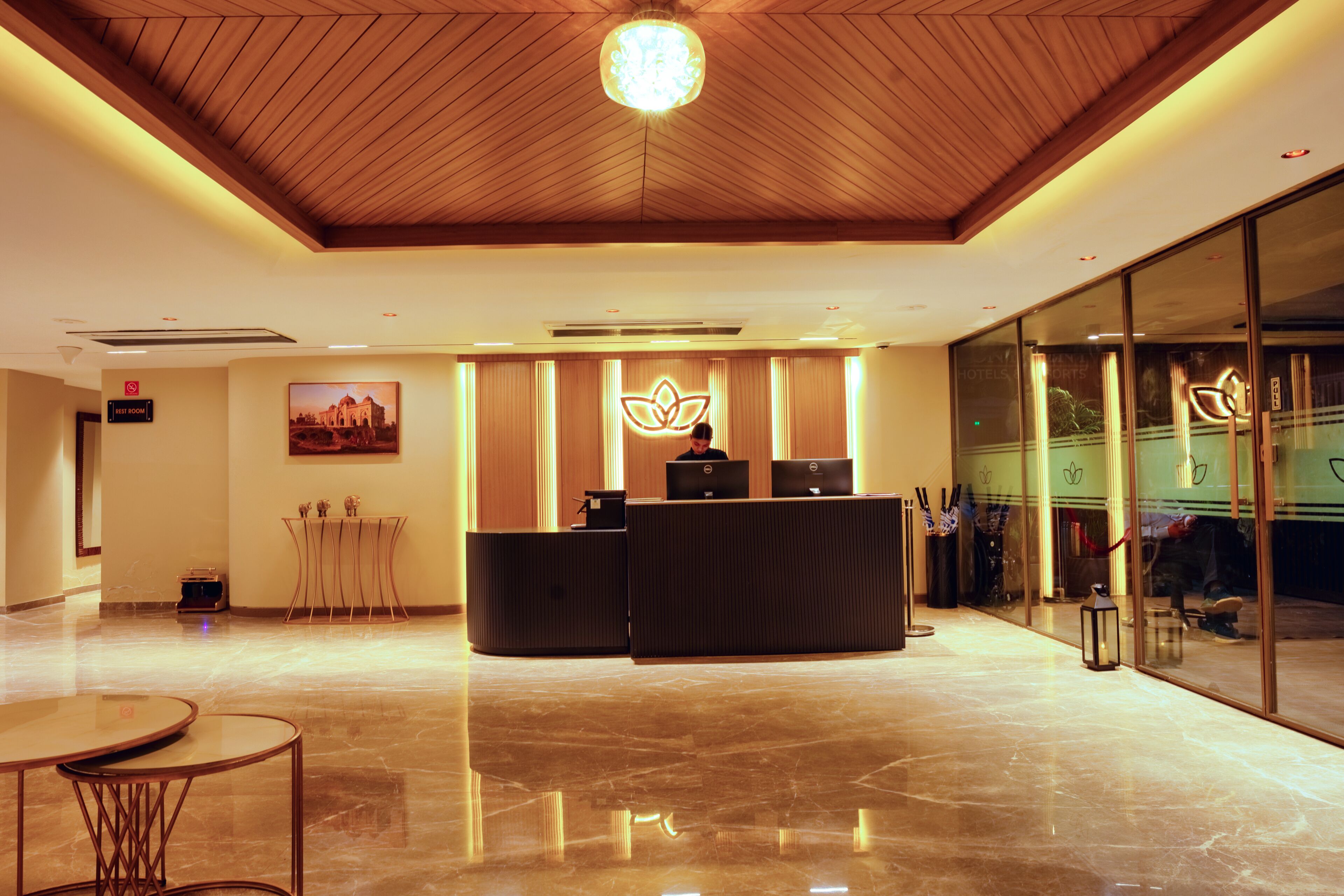 A hotel reception area with a wooden ceiling, a reception desk, a seating area, and a large window.