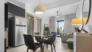 A modern kitchen with a built-in refrigerator, dining table with chairs, a ceiling fan, and a living area with a sofa and lamp. - NOK Modern 1BR With Terrace by Vistacana Rentals (Punta Cana)