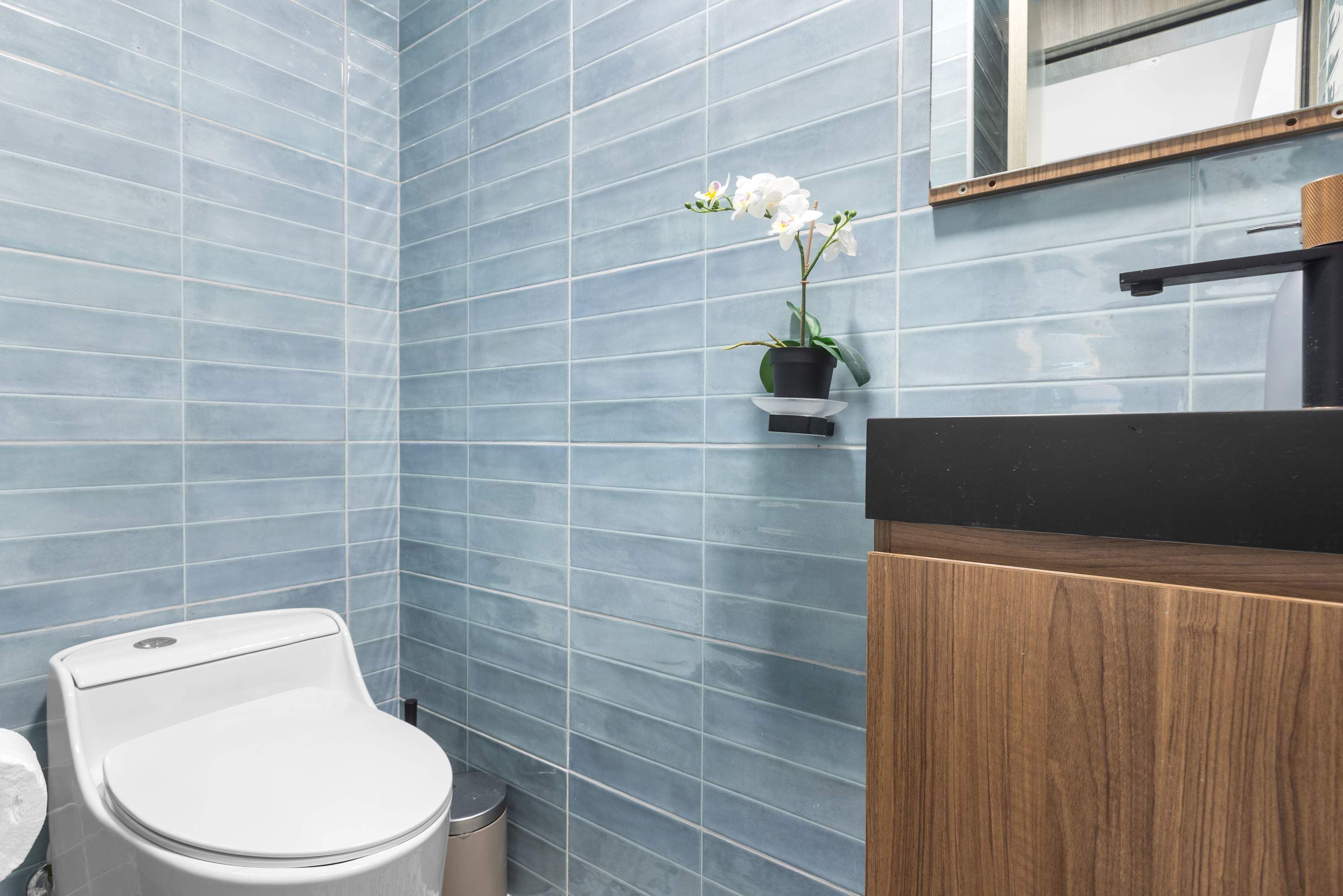 Un baño con inodoro, un cesto de basura, un lavabo con espejo y una orquídea en maceta.