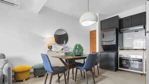 A compact kitchen with a microwave, oven, and modern appliances. There is a dining area with a table and chairs, and a sofa with a cushion. - NOK Modern 1BR With Terrace by Vistacana Rentals (Punta Cana)