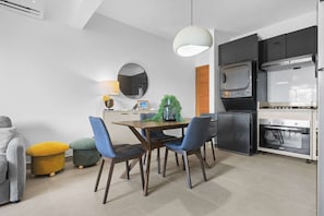 Eine kompakte Küche mit Mikrowelle, Backofen und modernen Geräten. Es gibt eine Essecke mit Tisch und Stühlen sowie eine Couch mit Kissen.