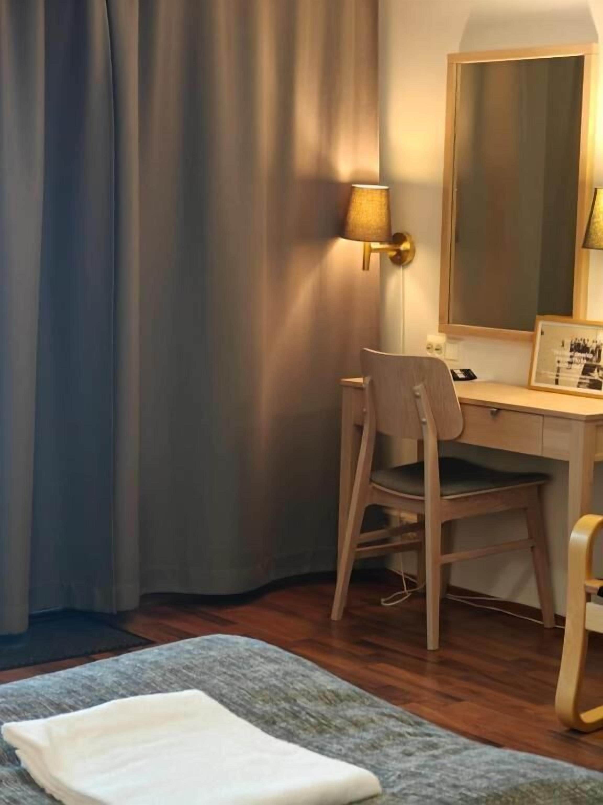 Ein Hotelzimmer mit Schreibtisch, Stuhl, Lampe, Spiegel und einem Bett mit Decke.