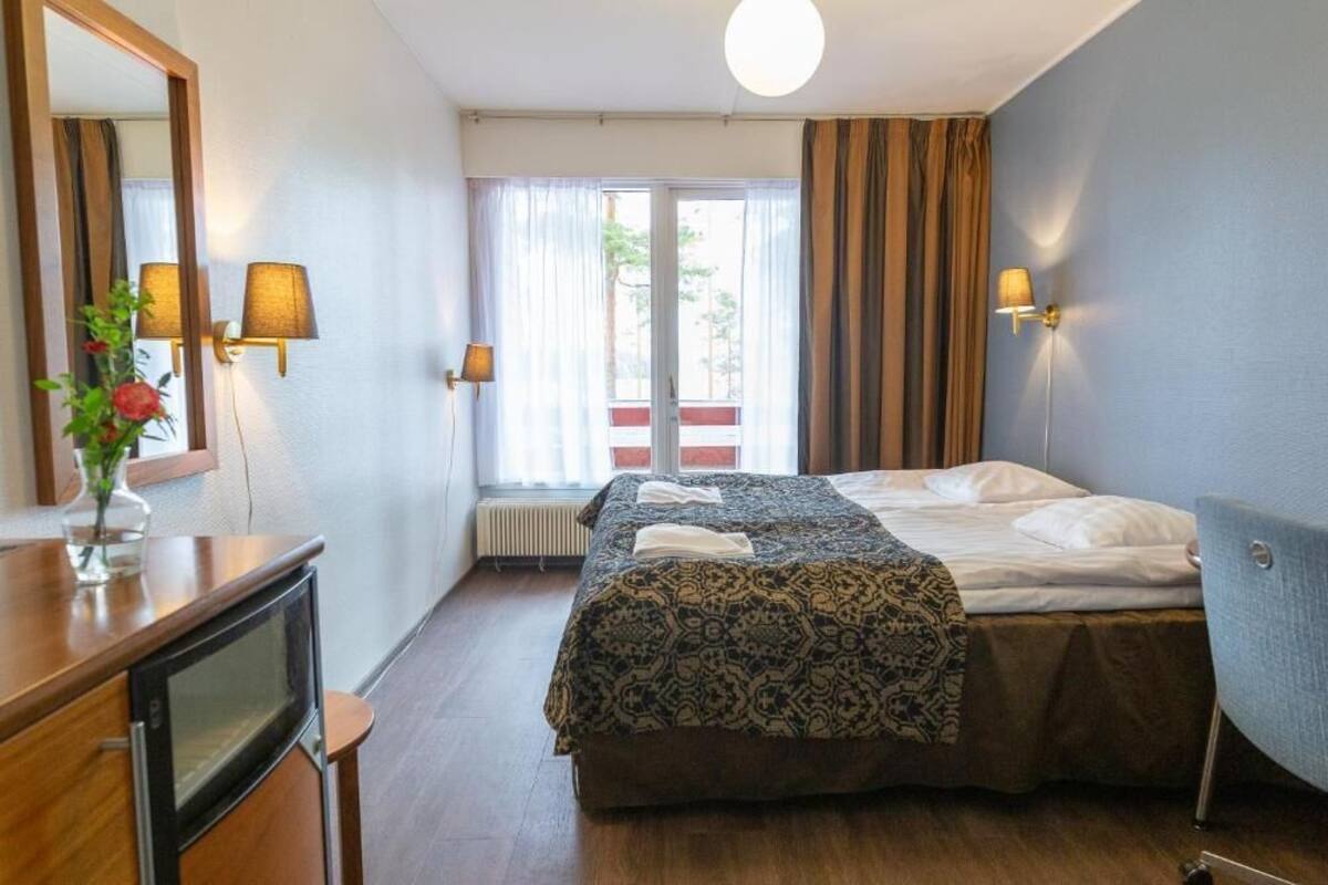 A hotel room with a bed, a desk with a computer, a mirror, and two wall-mounted lamps.