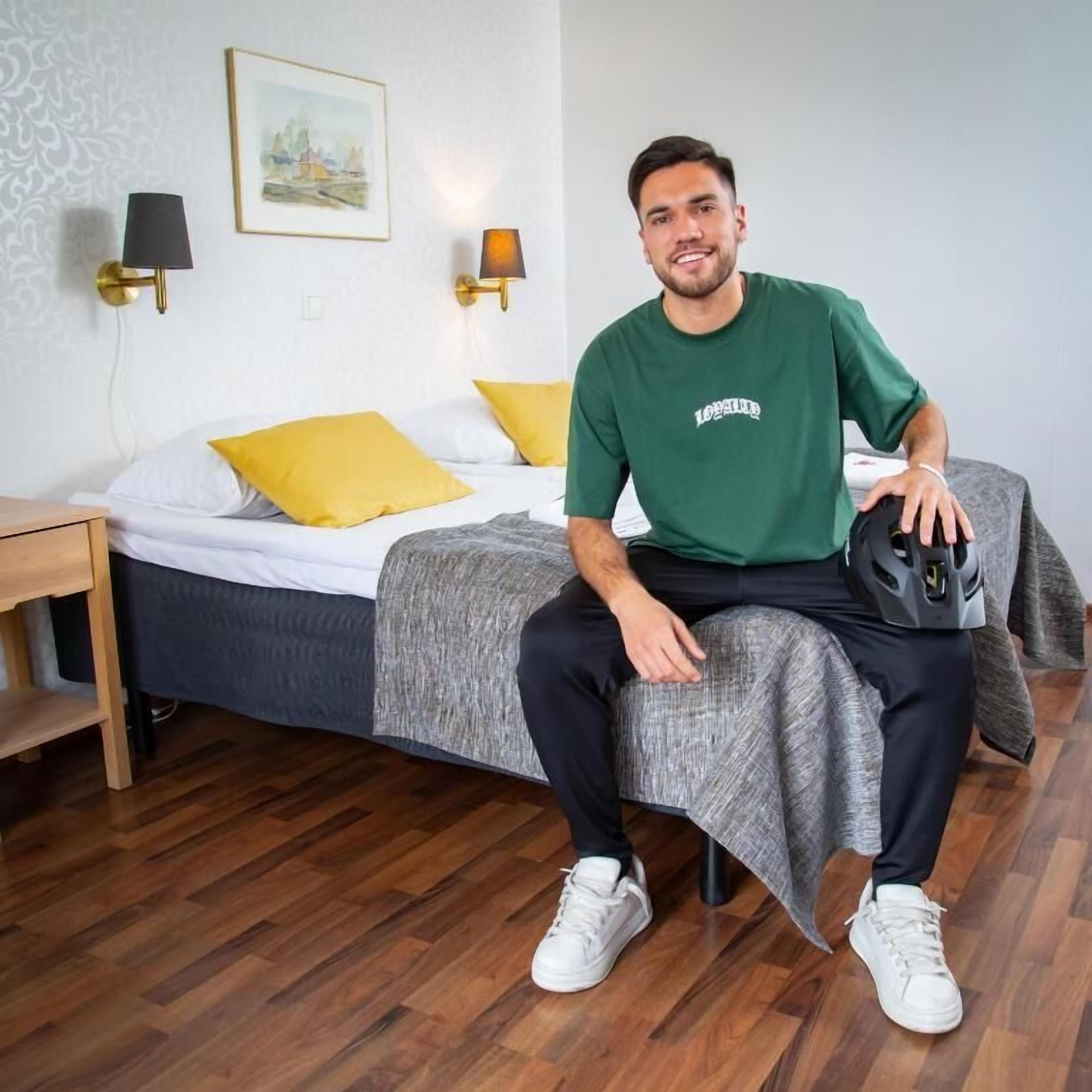 Een hotelkamer met een bed, nachtkastje, lamp en een lijst aan de muur.