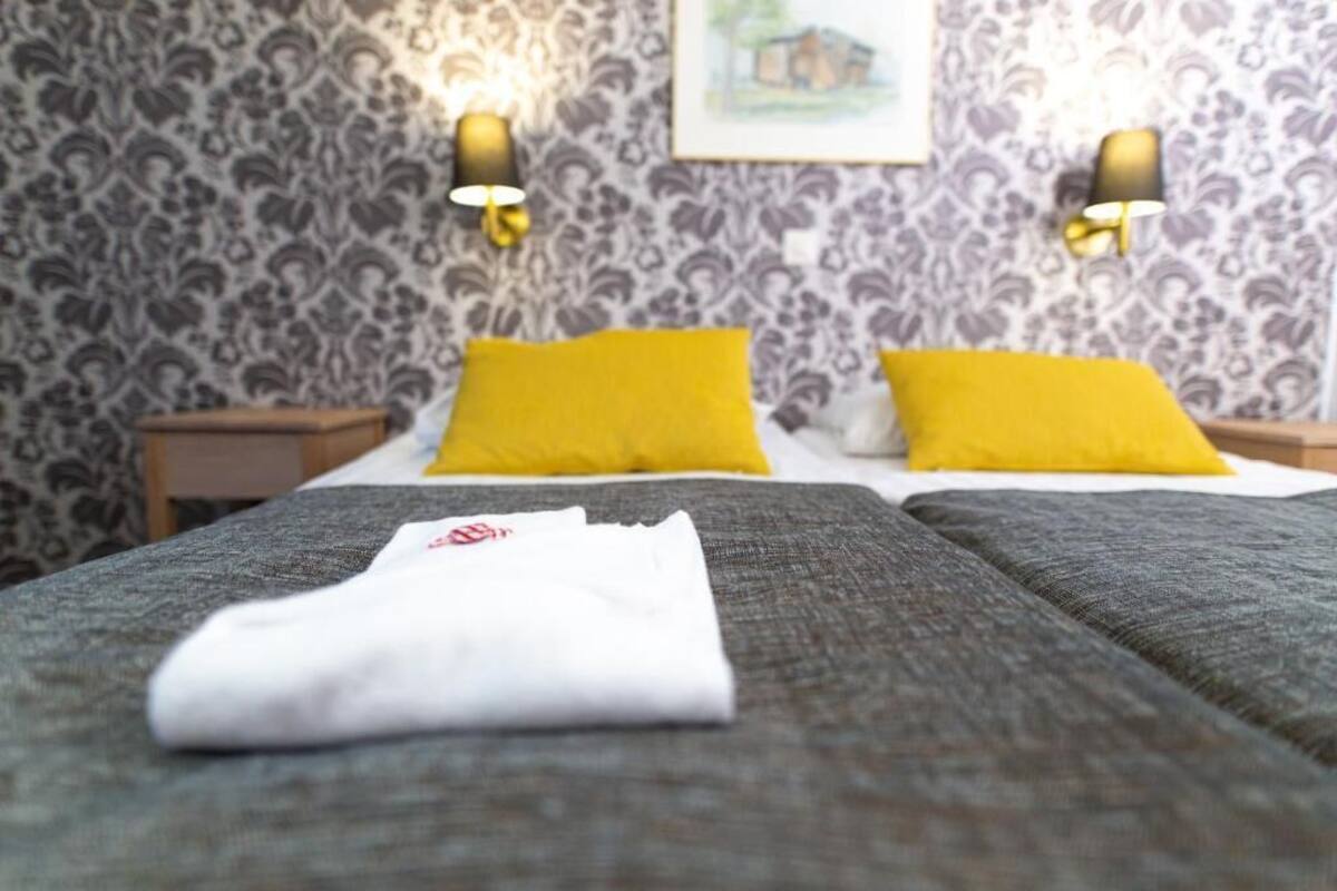 A hotel room with patterned wallpaper, two bedside tables with lamps, and a bed with two pillows.