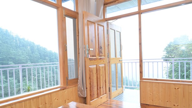 Un interior de madera con un ventanal grande, una puerta y vistas a un bosque.