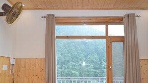 Una habitación con paredes de madera, un ventanal con cortinas, un banco de madera y un ventilador de techo.
