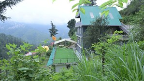 Una casa con techo verde, rodeada de abundante vegetación y montañas al fondo.