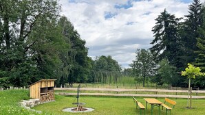 Un espacio al aire libre con césped, una estructura de madera, un pozo de fuego y un banco.