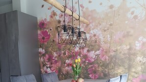 Un comedor con una mesa gris, sillas tapizadas en gris, una lámpara colgante y un fondo de papel tapiz floral.