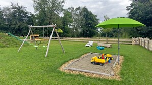 Un parque infantil con columpios, un arenero y vehículos de juguete.