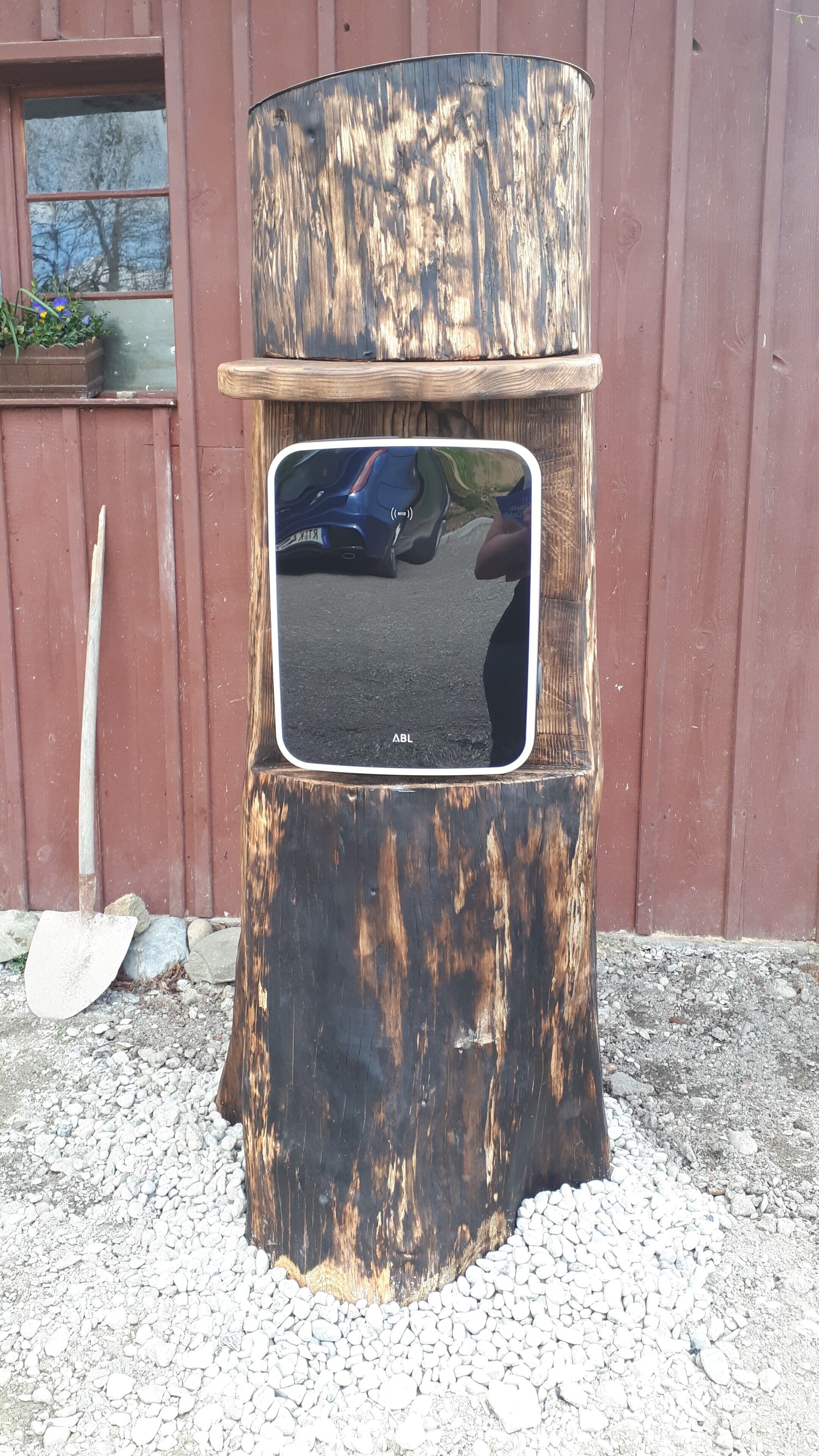 A rustic wooden structure with a reflective surface, possibly a mirror or a decorative panel, mounted on a tree stump.