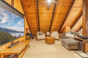 Une chambre mansardée chaleureuse avec un plafond en bois, une grande fenêtre donnant sur un paysage montagneux, un lit en bois et un petit bureau avec une chaise.