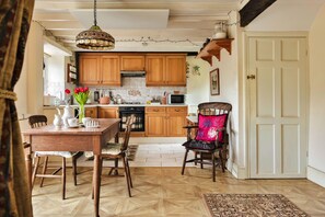 A kitchen with wooden cabinets, a dining table with chairs, a hanging light fixture, and a door. - Vine Barn (Bellerby)