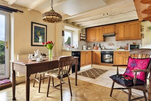 A kitchen with wooden cabinets, a dining table with chairs, a hanging light fixture, and a window with a view. - Vine Barn (Bellerby)