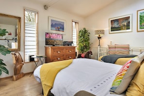 Ein Schlafzimmer mit einem Bett, einem Schminktisch, einem Fernseher, einer Pflanze und Kunstwerken an den Wänden.