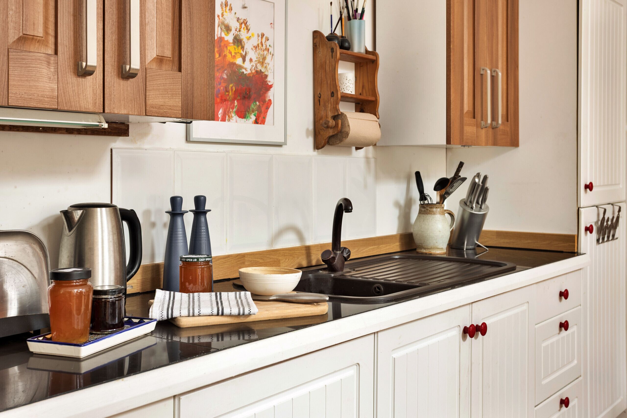 A kitchen with wooden cabinets, a stainless steel sink, and various kitchen utensils.