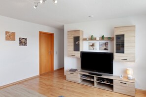 Uma sala de estar moderna com televisão de tela plana, móvel de entretenimento em madeira e uma porta.