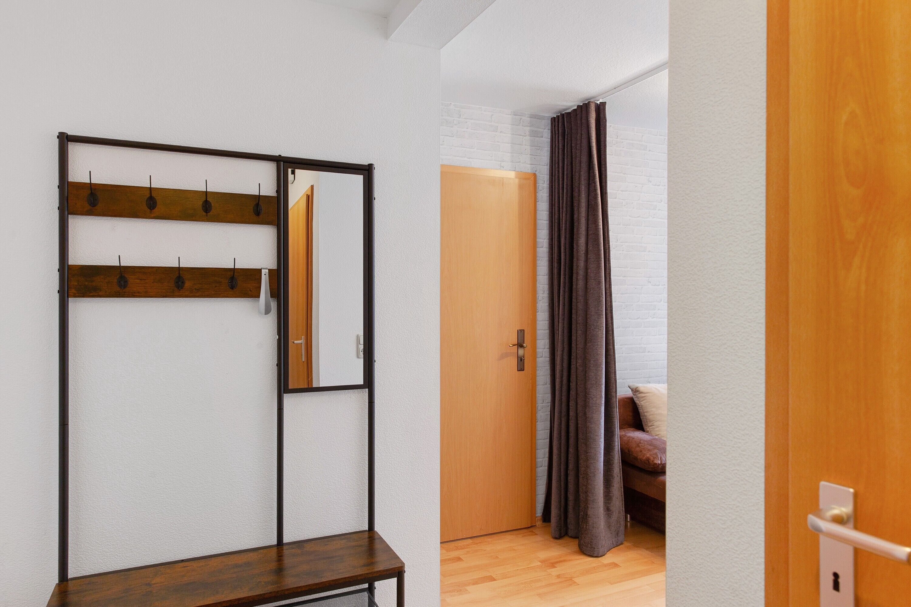 Una habitación con un banco de madera, un perchero, una puerta y una cortina marrón.