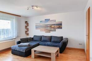 Uma sala de estar moderna com um sofá seccional, uma mesa de centro de madeira e uma obra de arte com tema de praia.