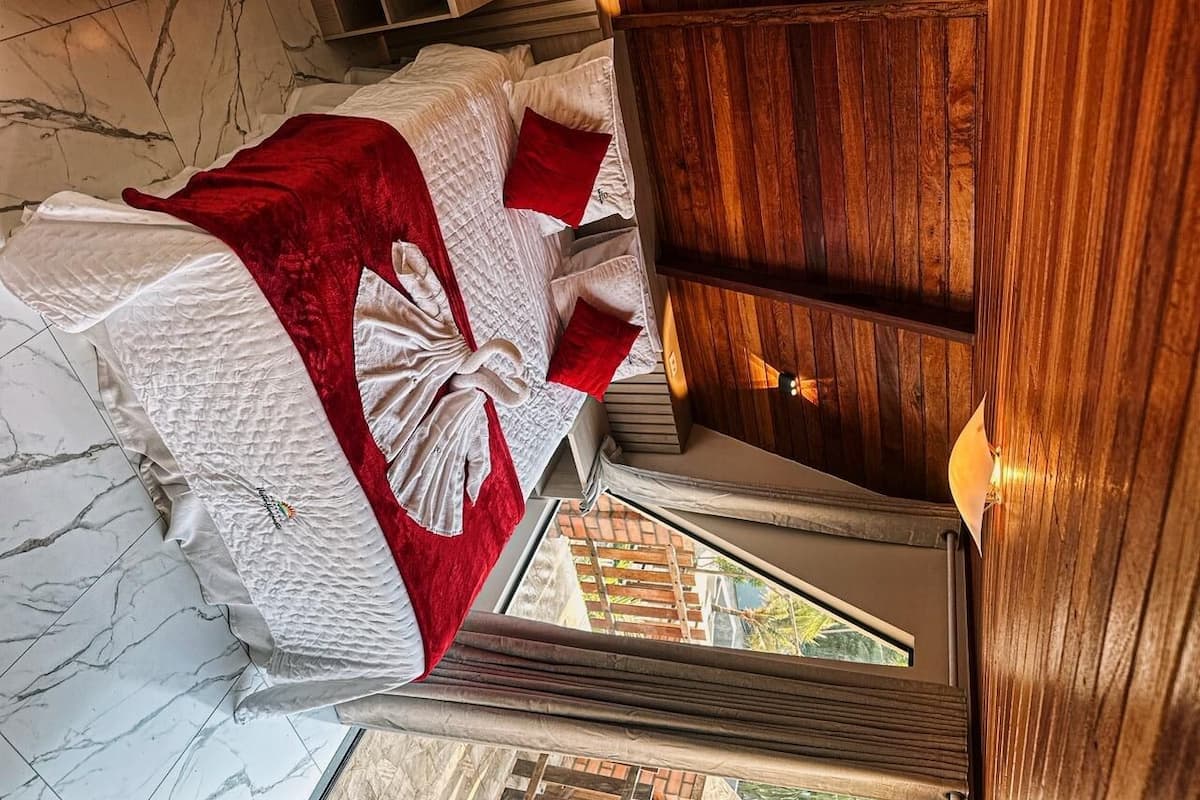 Una cama con una manta y almohadas rojas, un cabecero de madera y vistas al exterior a través de una ventana.