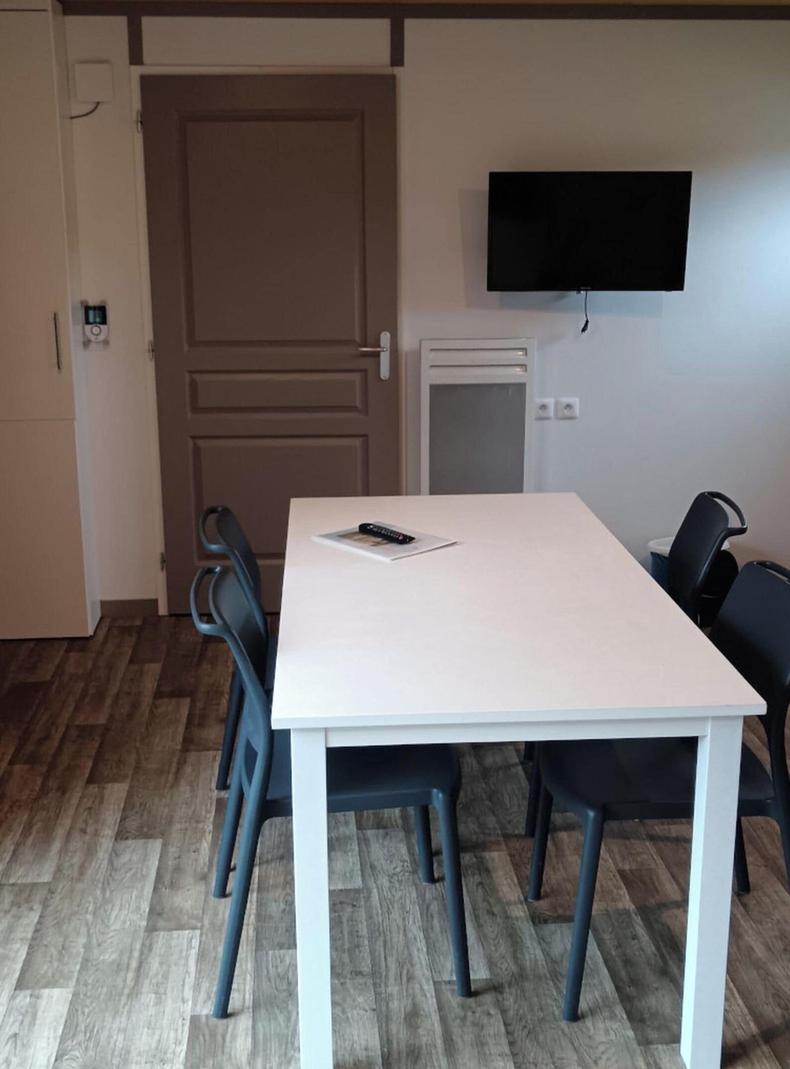 A room with a white table, four chairs, a television on the wall, and a door.