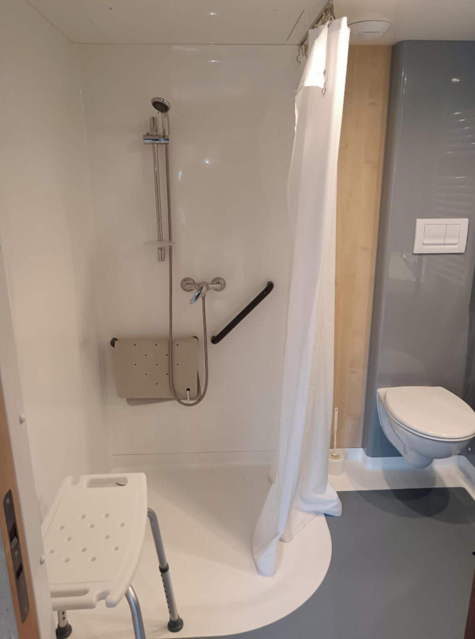A bathroom with a shower, toilet, and a wheelchair-accessible bench.