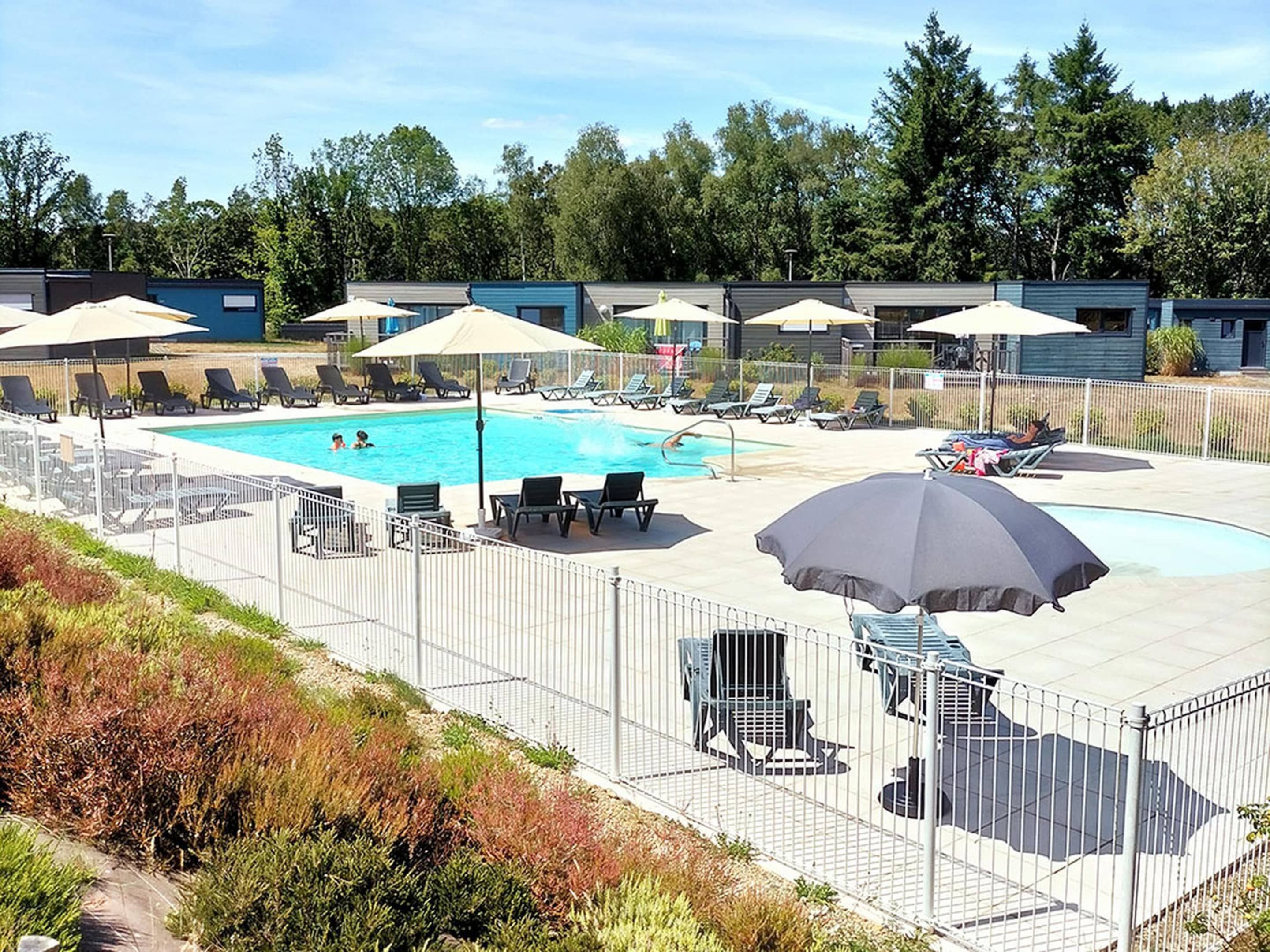 A swimming pool area with lounge chairs and umbrellas, surrounded by a fence.