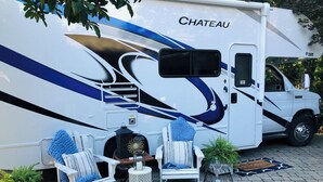 Ein großes Wohnmobil namens 'Chateau' mit einem überdachten Sitzbereich, einem kleinen Tisch und einem dekorativen Spiegel.