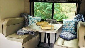 Ein gemütliches Wohnmobil-Interieur mit Esstisch, gepolsterten Sitzgelegenheiten und Blick ins Grüne.