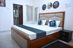 A bedroom with a bed, a nightstand, a bathroom with a shower, and a wall with three decorative plates. - Shri Jee Kunj Homestay (Varanasi)