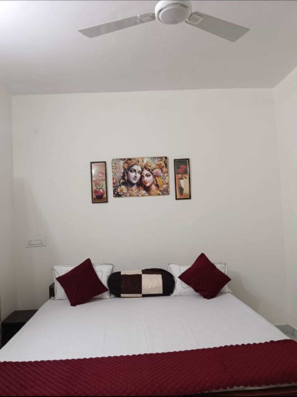 A bedroom with a bed, a ceiling fan, and three framed artworks on the wall. - Shri Jee Kunj Homestay (Varanasi)