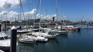 A marina with multiple sailboats docked, a clear sky, and a distant shoreline with buildings. - Zeebrugge Sea View Family-friendly the Beach (Bruges)