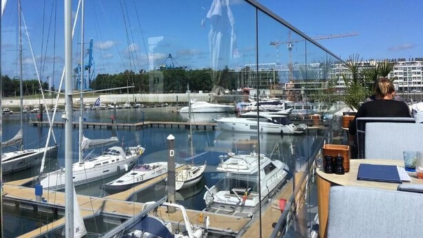 A marina with boats docked, a crane in the background, and a person seated at a table. - Zeebrugge Sea View Family-friendly the Beach (Bruges)