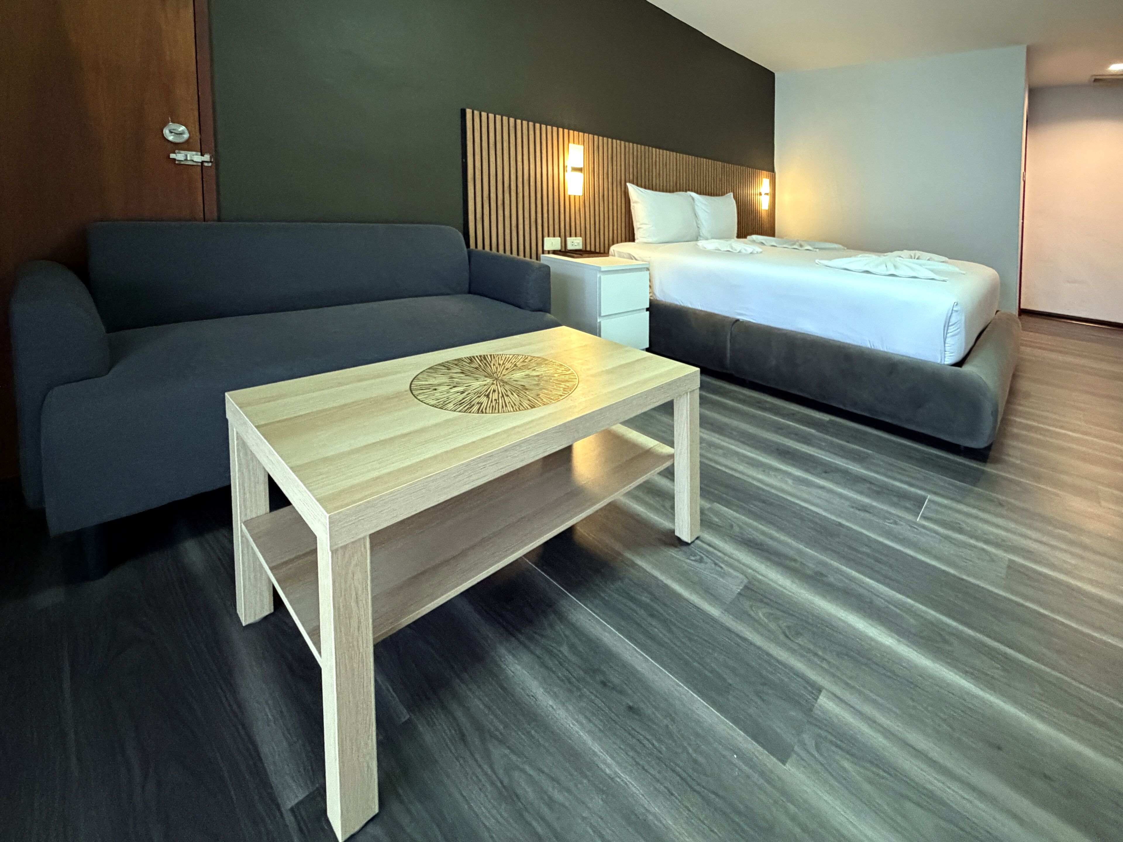 Quarto de hotel moderno com sofá, cama, mesa de centro de madeira e mesa de cabeceira.