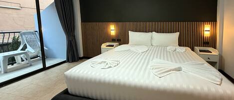 A hotel room with a large bed, two bedside tables, a window with a view, and a balcony with a chair and table.