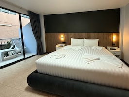 A hotel room with a large bed, two bedside tables, a window with a view, and a balcony with a chair and table.