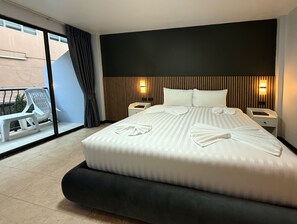 A hotel room with a large bed, two bedside tables, a window with a view, and a balcony with a chair and table.