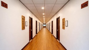 A long, narrow hallway with wooden floors and doors on both sides, leading to a bright room at the end.