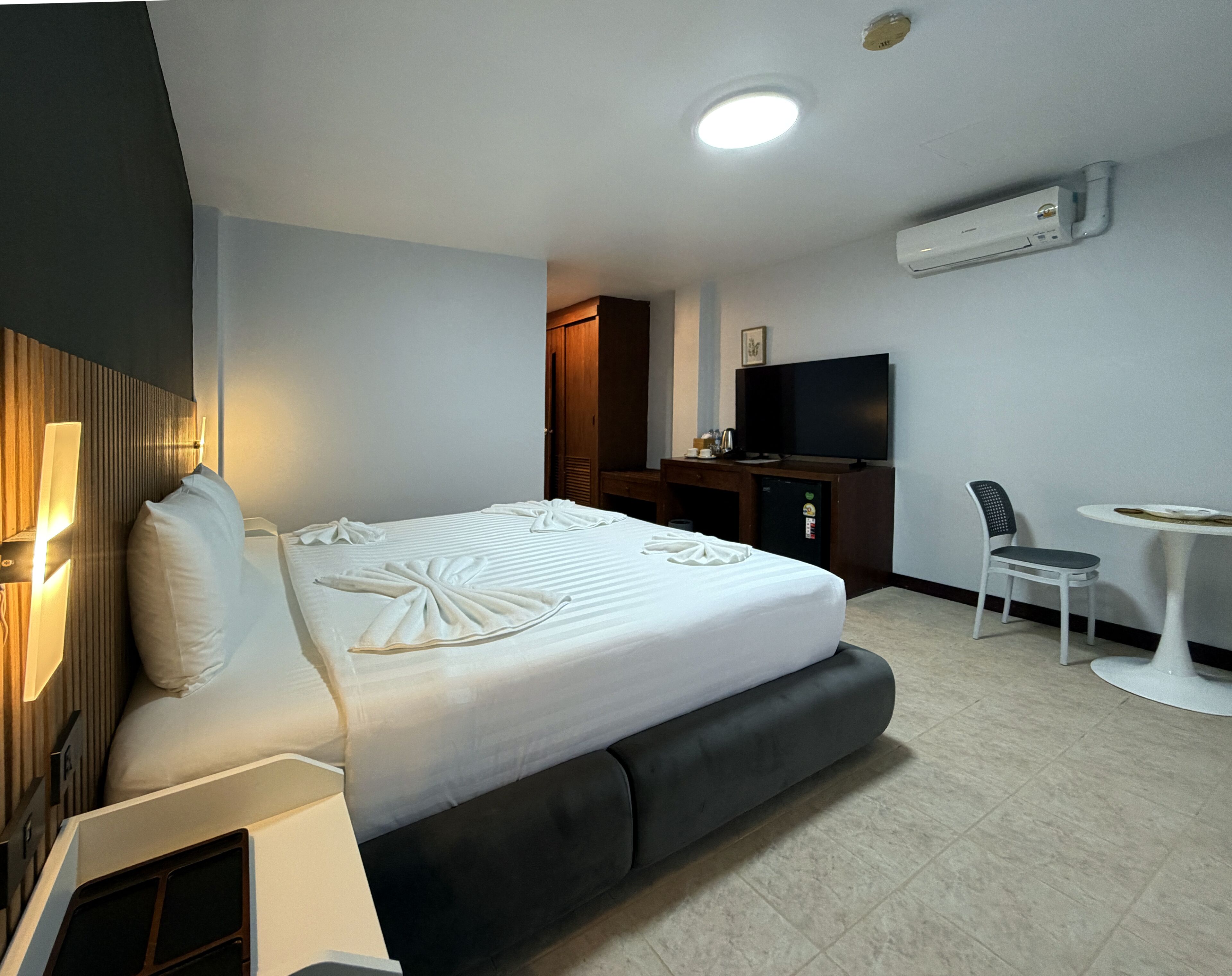 A hotel room with a bed, a desk, a chair, a television, and an air conditioning unit.