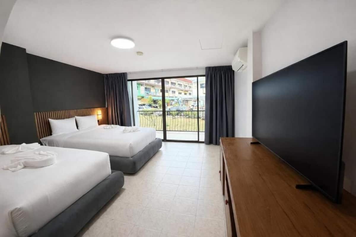 A hotel room with two beds, a TV, a balcony with a view, and a wooden dresser.