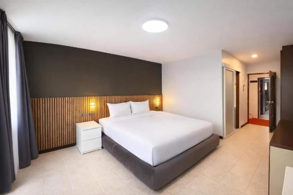 A modern hotel room with a large bed, bedside tables, a wooden headboard, and a small desk.